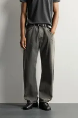 Jeans loose fit de hombre en denim de algodón color gris oscuro con efecto lavado. Presenta perneras con costuras giradas hacia los tobillos, tiro medio, cierre frontal con botones y bolsillos frontales con bolsillo cerillero.