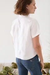 Blusa de lino verde de manga corta y corte recto, con cuello alto con volado y cierre frontal cruzado con botoncitos dorados.