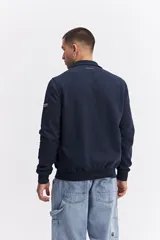 Campera de estilo deportivo con cierre frontal, confeccionada en una combinación de nylon y algodón. Presenta un diseño con paneles texturizados en las mangas, cuello alto y un parche decorativo con coordenadas en el pecho.