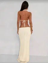 Vestido largo de tejido de punto color crema, con escote halter, espalda descubierta, abertura en la falda y detalle de aro dorado en el pecho.