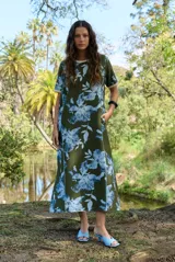 Vestido midi verde militar con estampado floral en tonos celestes, de manga corta, cuello redondo y bolsillos laterales.
