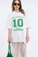 Remera oversize gris oscuro con cuello en V y mangas cortas. Presenta una estampa frontal estilo universitario con el número "09" y las inscripciones "MVD", "UY" y "PIMENTÓN ACTIVE" en tonos celestes y blancos.