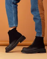 Botinetas de cuero negro con diseño combinado en gamuza y cuero texturizado. Presentan cierre frontal central, suela track dentada con costuras visibles en contraste y caña media.