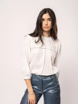 Blusa blanca de algodón con escote redondo, manga tres cuartos y silueta oversized. Presenta bordados y texturas combinadas.