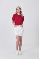 Falda mini de jean color blanco con costuras en contraste color ocre. Presenta un detalle de trenzado decorativo en los bolsillos delanteros y ruedo desflecado.