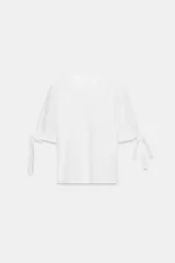 Camiseta de cuello redondo confeccionada en algodón, con mangas cortas abullonadas de tejido bordado perforado y detalle de lazadas en los puños.