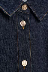 Cazadora de denim azul oscuro con cuello solapa, manga larga, cierre frontal con botones metálicos y bolsillos delanteros de plastrón.