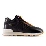 Championes urbanos New Balance modelo 574, color negro con detalles en beige y suela de goma color caramelo. Confeccionados con tecnología Cordura, presentan cordones bicolores en amarillo y rojo, logo N lateral y entresuela con tecnología ENCAP para mayor amortiguación.
