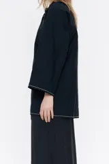 Camisa blanca de algodón, de corte línea A, con cuello mao con lazo a modo de cierre y manga larga ancha con pespunte bordado en puños.