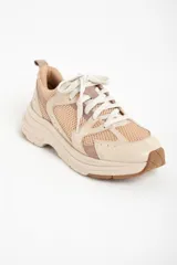 Zapatilla deportiva de mujer con plataforma gruesa, combinando paneles de malla transpirable color beige claro y superposiciones en tonos rosa viejo y crema. Cordones blancos y suela de goma color caramelo.