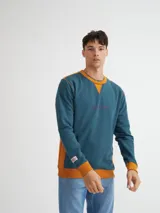 Buzo azul con cuello redondo, mangas largas y puños y bajo acanalados. Presenta bloque de color naranja en hombros y laterales, y estampado frontal con texto en color borgoña.