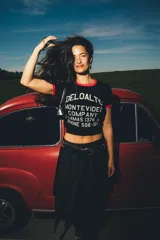 Remera tipo baby tee negra con ribetes rojos en cuello y mangas, y estampa frontal blanca con texto de marca y diseño de estilo vintage.