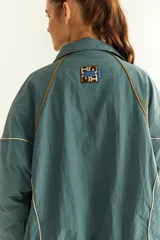 Campera rompevientos beige de nylon con diseño oversize, cuello alto, cierre frontal negro y detalles de costuras y ribetes en contraste.