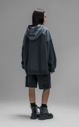 Hoodie oversize de algodón con diseño bicolor en gris oscuro y gris medio. Presenta capucha forrada, mangas raglán con recortes técnicos y un bolsillo frontal tipo canguro con un compartimento adicional con solapa.