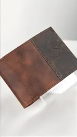 Billetera masculina confeccionada en cuero, con diseño bicolor en tonos marrón claro y oscuro. Presenta un detalle grabado de un búho en la parte frontal.