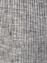 Camisa a rayas verticales grises y blancas, de lino, con cuello clásico, cierre frontal con botones, mangas abullonadas 3/4 con puños elásticos negros y corte holgado.