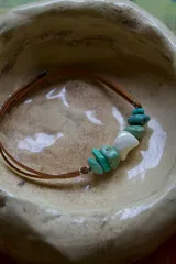 Gargantilla de cuero sintético marrón con cuentas de nácar y piedras turquesas.