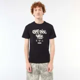 Remera negra de algodón con diseño estampado de estilo graffiti en el pecho con texto en blanco.
