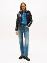 Campera puffer ultraliviana de color negro con acabado brillante, diseño acolchado horizontal y capucha. Presenta cierre frontal de cremallera, bolsillos laterales con cierre y logo engomado de Tommy Hilfiger en la manga. Confeccionada en nailon reciclado con corte regular.