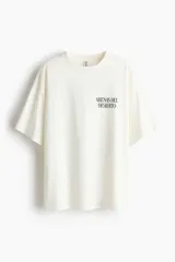 Remera oversized de punto suave de algodón, color blanco, con cuello redondo acanalado, hombros caídos y diseño estampado en el frente con la frase 'Arenas del Desierto'.