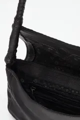 Cartera tipo baguette de cuero vacuno negro, con detalles de tachas metálicas doradas y plateadas en la solapa y borde trenzado. Cuenta con una correa de hombro trenzada.
