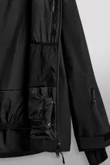 Cazadora deportiva de esquí en color negro, confeccionada en tejido técnico impermeable de tres capas con costuras y cremalleras termoselladas. Cuenta con capucha ajustable, ventilación en axilas, puños con ajuste de tira adherente y puño interior elástico con abertura para el pulgar. Incluye sistema de rescate RECCO y faldón interior para protección contra el frío.