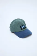 Gorra tipo dad hat de pana combinada en bloques de color verde y azul, con visera curvada y un parche bordado en el frente con diseño de montañas y la inscripción "UNIFORM".