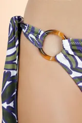 Bombacha de bikini con diseño asimétrico, presenta un detalle de argolla circular en uno de los laterales y tiras para anudar. Posee un estampado orgánico en tonos verde oscuro y azul sobre fondo blanco.
