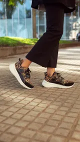 Championes deportivos de cuero en tonos marrón, tostado y marrón oscuro, con detalles de estampado animal print de leopardo en el lateral, suela gruesa blanca y cordones elásticos.