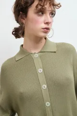 Camisa negra de tejido de punto acanalado, con cuello tipo polo y botones blancos.