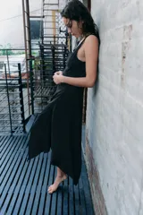 Vestido midi de viscosa color negro, sin mangas, con escote en pico adornado con encaje a tono. Presenta un detalle de nudo drapeado en la cintura y bajo asimétrico.