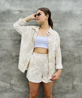 Conjunto de camisa y short beige con estampado de hojas, camisa de manga larga con botones y short con bolsillos laterales.