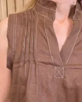 Musculosa marrón sin mangas, con cuello alto, escote en V y detalles de pespuntes blancos en contraste. Presenta pliegues y alforzas frontales.
