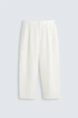Pantalón blanco de corte relajado (relaxed fit) con pliegues frontales, bolsillos laterales y bolsillos traseros de vivo. Cierre frontal con cremallera y botón.