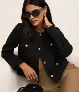 Chaqueta de manga larga confeccionada en tejido tweed color negro, con cuello redondo, cierre frontal mediante botones metalizados dorados y bolsillos frontales con solapa y botones a juego.