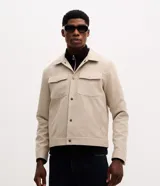 Campera estilo trucker de gamuza sintética color beige, con cuello clásico, cierre frontal con botones metálicos y dos bolsillos delanteros con solapa en el pecho.