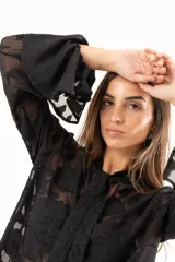 Blusa negra de tejido semitransparente con diseño floral en relieve, cuello alto con lazo frontal y mangas largas con volados en los puños.