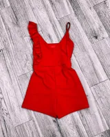 Mono corto blanco con escote en V, breteles finos y un volado en el hombro izquierdo.