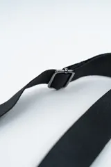 Bandolera de diseño rectangular en color negro, confeccionada en material texturizado. Cuenta con una correa de hombro ajustable y extraíble, cierre superior y tiradores laterales decorativos.