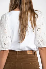 Remera de algodón color rosado con mangas cortas abullonadas de broderie con diseño floral calado. Presenta cuello redondo y costura vertical central en el frente.