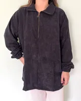 Buzo negro de pana con cierre metálico en el cuello, corte holgado y mangas largas con puños elásticos.