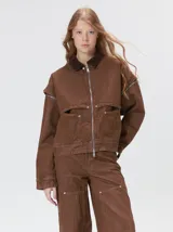 Campera de denim grueso color marrón, con cuello de pana, cierre frontal y mangas desmontables. Presenta un diseño con canesú en el pecho y dos bolsillos de parche cuadrados.