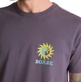 Remera Roark de manga corta en color violeta, con diseño gráfico pequeño en el pecho que representa un sol y olas con la inscripción 'Roark'.