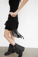 Falda pantalón de tiro bajo en color negro, con cintura drapeada y detalle de tira lateral colgante. Presenta un diseño con volantes en el bajo y cierre de cremallera metálica.