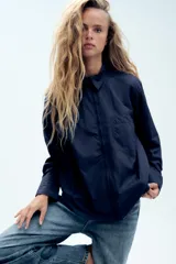 Camisa oversize de nylon color azul marino, con cuello solapa, manga larga, bolsillo de parche en el pecho y cierre frontal con cremallera.