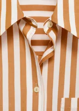 Camisa de corte oversize con diseño de rayas verticales en tonos blanco y naranja. Presenta cuello camisero clásico, cierre frontal con botones, bolsillo de parche en el pecho y mangas largas con puños abotonados.