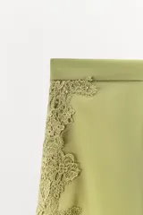 Shorts de tiro alto confeccionado en tejido satinado color verde oliva, con cintura elástica, bajo con volantes y aberturas laterales decoradas con aplicaciones de encaje a tono.