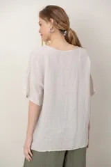 Blusa de lino color blanco, de corte amplio, con escote redondo, mangas cortas y detalle de guarda calada horizontal en la parte inferior.