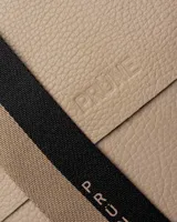 Bandolera color beige con correa ancha de tela negra con el nombre de la marca en blanco.