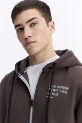 Campera con capucha y cierre frontal, color crema, con bolsillo canguro. Presenta un estampado de texto en el pecho y detalles en el puño.